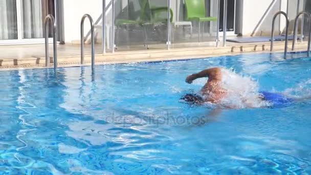 Sportlicher muskulöser Mann schwimmt im Pool. Junger Kerl, der an einem sonnigen Tag über das Hotelbecken schwebt. Sommerferien oder Urlaubskonzept. Zeitlupe in Nahaufnahme — Stockvideo