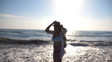 Genç kız bikini ve denize sıfır plaj üzerinde iplik sırt çantası ile gömlek. Hayattan zevk ve having fun Coast'ta güneşli bir günde şapkalı güzel bir kadın. Yaz tatili ya da tatil. Ağır çekim