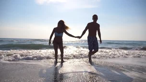 Bella coppia sorridente innamorata che cammina vicino al mare. Gli amanti si divertono insieme in vacanza. Concetto di amore e felicità. Rallentatore — Video Stock