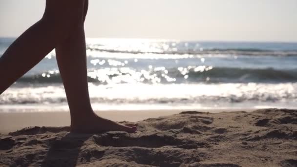 Piedi femminili camminando sulla spiaggia del mare in una giornata di sole con onde sullo sfondo. Gambe di giovane donna che calpesta la sabbia. Vacanza estiva o concetto di vacanza. Vista laterale Rallentatore Close up — Video Stock