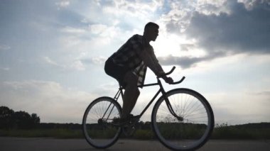 Adam arka plan güzel günbatımı gökyüzüne vintage bisiklet sürme silüeti. Sportif adam ülkede yol Bisiklete binme. Erkek bisikletçi sabit binicilik bisiklet dişli. Sağlıklı aktif yaşam tarzı ağır çekim