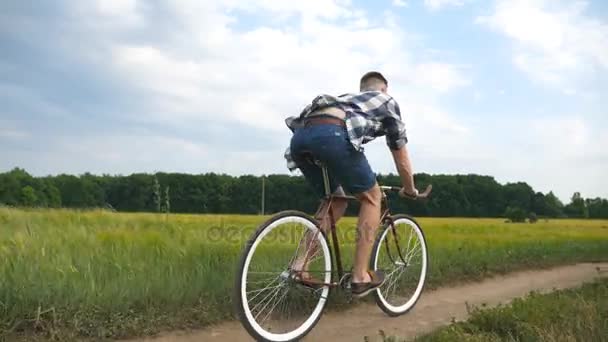 Молодой человек ездит на винтажном велосипеде по сельской дороге через поле. Спортивный парень катается на велосипеде по деревенской тропе. Мужчина велосипедист катается на велосипеде в сельской местности. Здоровый активный образ жизни — стоковое видео