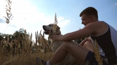 Genç adam çayır, yeşil çimenlerin üzerinde oturan ve köpeğini okşuyordu. Erkek sahibi ile birlikte onun labrador veya doğa adlı golden retriever vakit. Yavaş hareket kapatmak