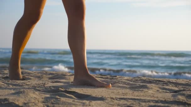 Primo piano del piede femminile che calpesta la sabbia con onde marine sullo sfondo. Bella donna che cammina sulla costa a piedi nudi in una giornata di sole. Concetto di vacanza estiva o vacanza. Rallentatore — Video Stock