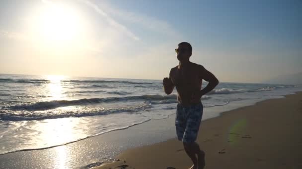 Sportovní mladík běží na pláži u moře během východu slunce. Sportovní kluk zaběhat podél pobřeží oceánu. Mužské sportovce vykonávající venkovní. Zdravý aktivní životní styl. Detailní záběr Zpomalený pohyb — Stock video