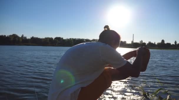 Joven parado en el yoga posan en un embarcadero de madera en el lago. Atleta balanceándose en una pierna. Tipo deportivo haciendo ejercicio de estiramiento al aire libre. Concepto de estilo de vida activo saludable. Vista trasera trasera Primer plano — Vídeos de Stock