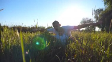 Genç Baba ve yeşil çimenlerin üzerinde oturan ve oynarken küçük oğul portre uçak ellerini kaldırdı. Birlikte vakit ve doğanın keyfini bir aile. Arka plan, güneş ışığı. Düşük açılı görünümü kapatın