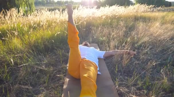 Vue de dessus du jeune homme couché sur le tapis à la prairie et pratiquant le yoga par une journée ensoleillée. Homme sportif faisant de l'exercice d'étirement sur le terrain. Paysage estival à l'arrière-plan. Mode de vie sain et actif Fermer — Video