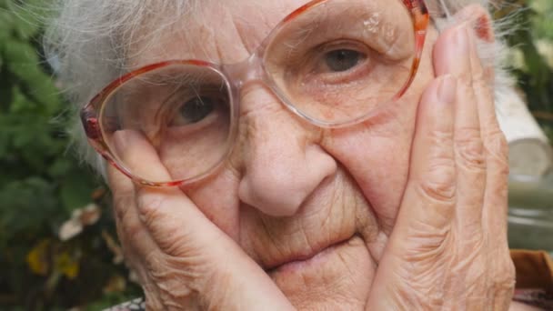 感情や気持ちで悲しい祖母の肖像画。老女屋外悲痛な表情でカメラ目線します。おばあちゃんは、彼女の顔に手を維持し、大きくため息をつきます。スローモーションを閉じる — ストック動画
