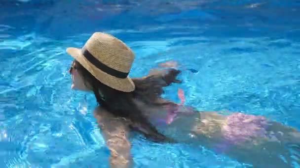 Молодая красивая девушка в солнцезащитных очках и шляпе плавает в бассейне. Женщина отдыхает в чистой теплой воде в солнечный день. Концепция летнего отпуска или отпуска. Закрыть Медленное движение — стоковое видео