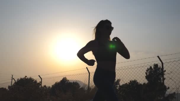 Після спортивної дівчини біг по сільській дорозі на сході сонця. Молода жінка бігає на відкритому повітрі вранці. Здоровий активний спосіб життя. Повільний рух — стокове відео