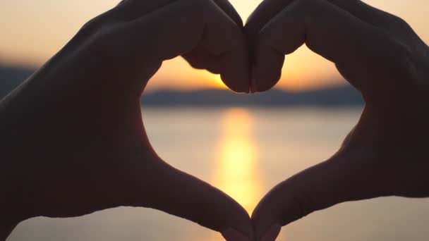 Silhouet van jonge vrouwelijke handen die hartvorm maken over zee achtergrond met prachtige zonsondergang. Begrip zomervakantie. Sluiten Slow motion — Stockvideo