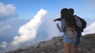 Dağın tepesinde dikilen iki genç turist ilerideki güzel manzaraya bakıyor. Adam kanyonun kenarındaki bir şeyi işaret ediyor. Arka plan Görünümü Yavaş çekim Kapat