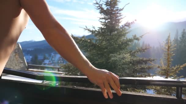 Вид збоку на невпізнаваного спортсмена, який стоїть на балконі і дивиться на красиву природу в сонячний день. Молодий чоловік насолоджується зимовими канікулами або відпусткою. Прекрасний краєвид. Крупним планом Повільний рух — стокове відео