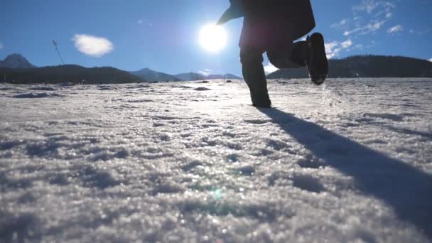 認識できない男は晴れた冬の日に雪のフィールドにジョギングします。雪に覆われた草原で走っている若い人。太陽の光と青空背景で。休日や休暇の概念。背面バック見るスローモーション — ストック動画