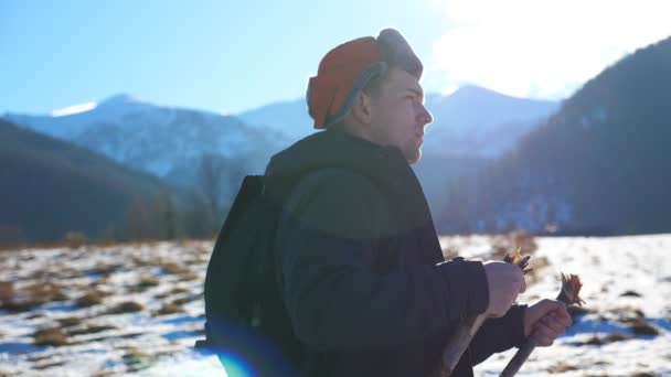 山岳地帯の雪上歩道に棒でノルディックウォーキングに行く若いハイカーの側のビュー。晴れた日にはスポーツマンが屋外で運動をする。健康的なアクティブライフスタイルの概念。スローモーション — ストック動画