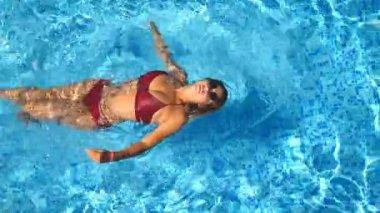 Genç kadın güneş gözlüğü ve kırmızı bikini arkadaki havuzda yüzme. Güzel kız otel Havzası güneşli günde yüzer. Yaz tatili veya tatil kavramı. En iyi görünümü kapatın