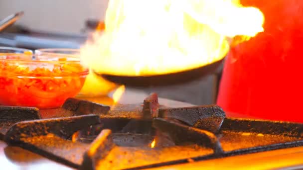 Невпізнаваний шеф-кухар готує страву в стилі флембе на сковороді в готельному ресторані. Чоловік готує смаження овочів у вогняній сковороді на газовій плиті вранці для туристів. Концепція приготування їжі. Вид збоку — стокове відео
