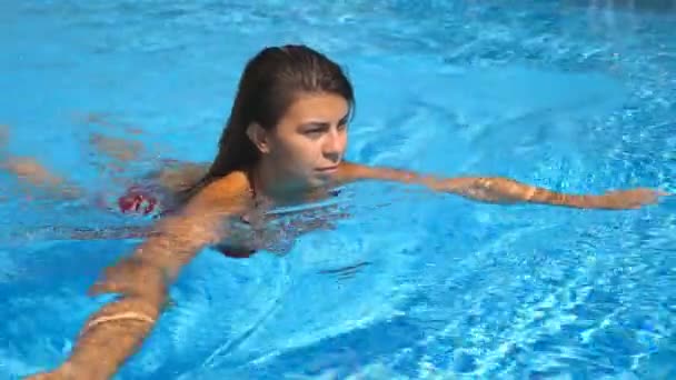さわやかな空のプールに泳ぎに若いの日焼けした女性の肖像画。晴れた日に澄んだ青い水でリラックスしてホテルの洗面器に浮いているブルネットの少女。夏休みや休日の概念 — ストック動画