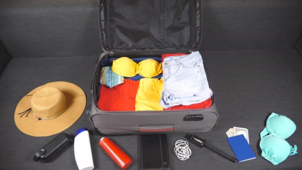 Одежда и вещи, наполняющие чемодан. Подготовка к летним путешествиям. Упаковка одежды и других принадлежностей к сумке. Планирование поездки или путешествия. Вид сверху — стоковое видео
