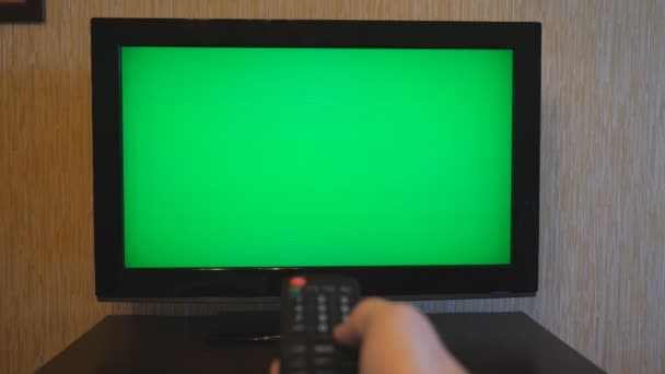 Мужская рука с помощью пульта дистанционного управления для переключения каналов на зеленом экране телевизора. Человек серфинга телевизионных каналов с ключом хромает. Точка зрения парня. POV Close up — стоковое видео