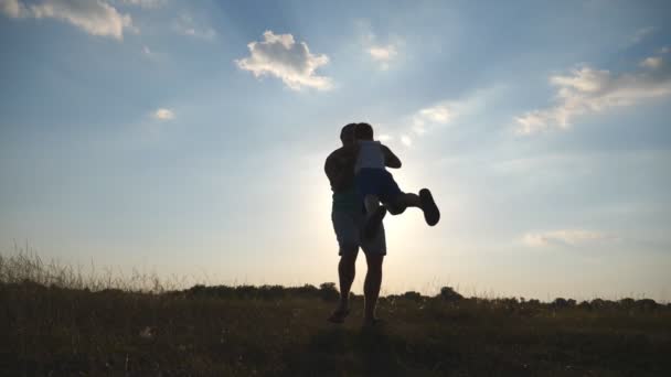 Padre che fa girare suo figlio in un prato in una giornata di sole. Papà ruota il bambino intorno alla natura. Famiglia che gioca sul campo al tramonto. Papà e bambino si divertono insieme. Chiudere rallentatore — Video Stock