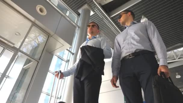 2 人の若いビジネスマン空港のターミナルで立っていると話しています。お互い屋内に会話中に楽しんで幸せな白人ビジネス男性。旅行の概念。スロー モーション ビューのローアングル — ストック動画