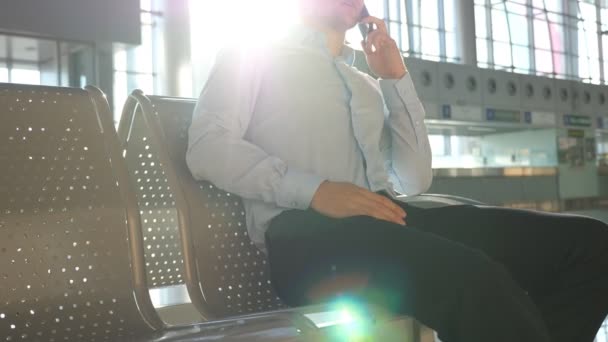 Jovem empresário falando ao telefone no aeroporto com bandeja de sol no fundo. Close up retrato de homem de negócios bonito em óculos de sol falando no celular no escritório. Lento movimento Fechar — Vídeo de Stock