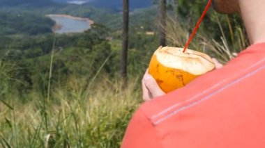 Genç güneşli gün içki taze hindistan cevizi su ile yeşil tepe üzerinde saman adam. Doğa zaman harcama ve güzel manzara zevk beyaz adam. Seyahat kavramı. Arka arka görünümü kapatın