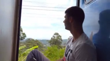 Tren hareket ve güzel doğa için bakan giriş yakınındaki oturan genç adam yan görünüm. Yolcu demiryolu taşımacılığı üzerinde sürme ve yaz seyahat zevk mutlu adam. Yakın çekim