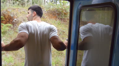 Arka giriş tren geçirilmesi ve açık kapılar yaslanmış duran mutlu adam arkadan görünüm. Genç yolcu demiryolu taşımacılığı üzerinde sürme ve güzel doğa arayan adam. Seyahat kavramı