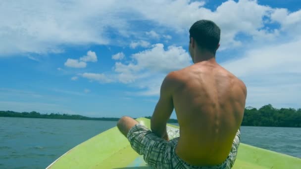 Hombre atlético joven sentado en la proa del barco y levantando las manos para disfrutar de la libertad. Chico deportivo feliz que busca hermoso paisaje de la naturaleza y relajarse en la cubierta del barco. Concepto de vacaciones o vacaciones. De cerca. — Vídeos de Stock