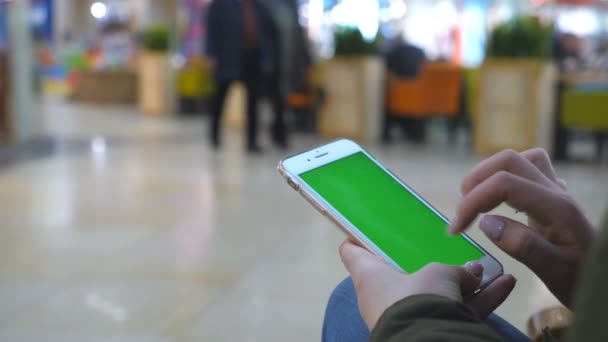 Mains féminines utilisant un smartphone moderne avec écran vert. Jeune fille assise au banc dans le centre commercial et tapant sur l'écran tactile du téléphone portable avec clé chromatique. Gros plan Mouvement lent — Video