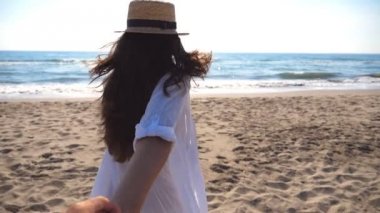 Erkek elini tutarak ve okyanus plaj üzerinde çalışan kız. Şapka çekme içinde genç kadın sevgilisi deniz kıyısında vurdu beni takip edin. Yaz tatil veya tatil kavramı. Bakış açısı Pov ağır çekim