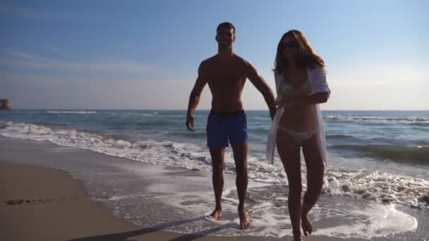Beautiful smiling couple in love walking near seashore. Lovers having fun together at vacation. Concept of loving and happiness. Slow motion — Stock Video