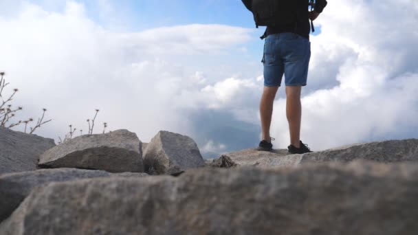 Caminhante masculino irreconhecível com mochila em pé no pico da montanha e desfrutando de uma bela paisagem. Céu nublado no fundo. Conceito de viagem. Visão traseira Visão traseira Movimento lento — Vídeo de Stock