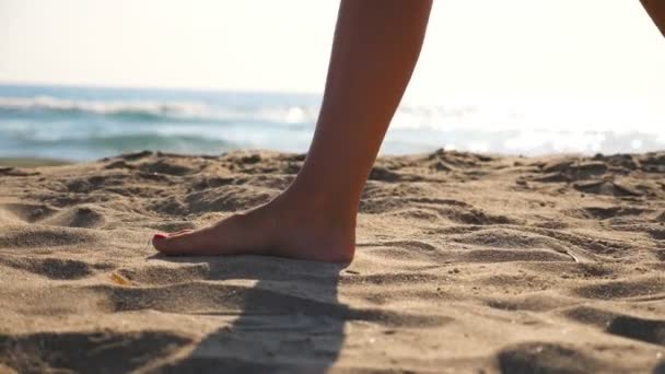 Close up de pés femininos andando sobre areia dourada na praia com ondas oceânicas no fundo. Pernas de uma jovem a pisar na areia. Menina descalça na costa do mar. Férias de verão. Movimento lento — Vídeo de Stock