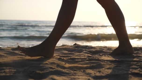 암컷 의발 이 해변에서 황금빛 모래 위를 걷고 있고, 뒤에는 파도가 밀려 있다. 젊은 여자의 다리가 모래 위로 내딛고 있어. 해변에 있는 발정난 소녀. 여름 방학이야. 느린 동작 — 비디오
