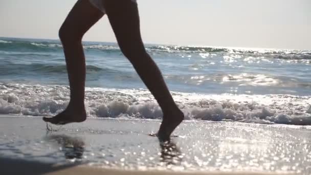 Primer plano de pies femeninos corriendo sobre arena mojada y agua de mar en la playa con olas al fondo. Piernas de una joven corriendo a la orilla. Chica descalza en la costa. Vacaciones de verano. Movimiento lento — Vídeos de Stock