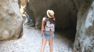 Sırt çantalı genç bir kadın kayalık boğazın arasında duruyor ve manzaraya hayran. Şapkalı tanınmayan yürüyüşçü doğa manzarasının tadını çıkarıyor. Kanyonu keşfeden dişi turist. Seyahat konsepti. Yavaş çekim