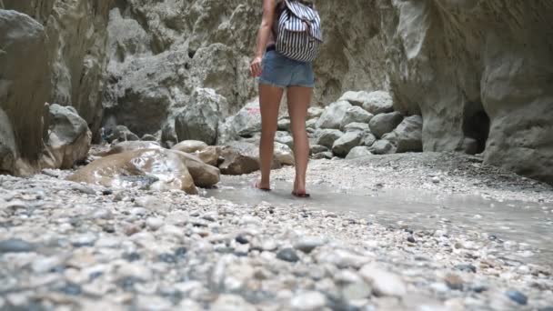 Неузнаваемая женщина с рюкзаком ходит по узкому каньону. Пешеход в шляпе прогуливается по скалистой местности и смотрит вокруг наслаждаясь живописным видом. Следуйте за женщиной турист исследуя ущелье. Медленное движение — стоковое видео