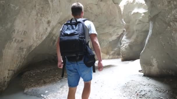 Giovanotto irriconoscibile con lo zaino che attraversa uno stretto canyon. Escursionista maschio esplorare gola rocciosa e ammirare viste panoramiche. Concetto di viaggio o riposo attivo. Rallentatore Indietro Close up — Video Stock