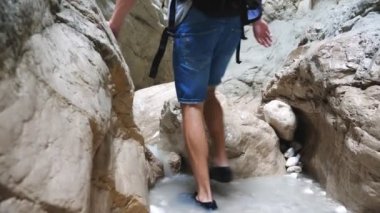 Sırt çantalı genç adam dar kanyonda yürüyor. Kayalık geçidi keşfeden erkek yürüyüşçü zorlu yolu aşıyor. Seyahat ya da aktif dinlenme kavramı. Yavaş çekim Arka plan