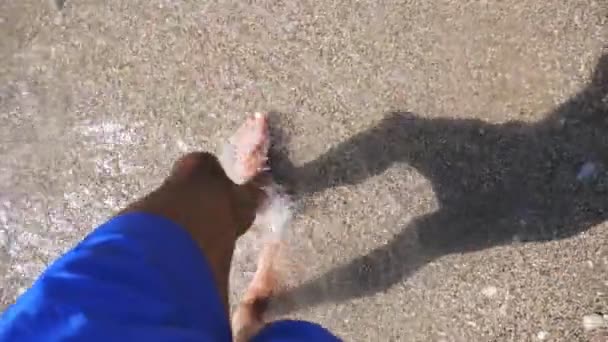 Hombre caminando lentamente descalzo en la costa en el día soleado. Pequeñas olas salpicando los pies de un joven paseando por la playa de guijarros del mar. Un tipo disfrutando de la recreación en la orilla del mar. Concepto de vacaciones de verano. Lento mo — Vídeos de Stock