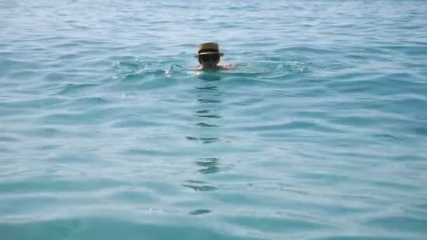 Mladá žena plavání na otevřeném moři těší letní dovolenou nebo dovolenou. Dívka v klobouku relaxující na exotickém letovisku plovoucí v azurově čisté vodě. Koncept cestování nebo letní dovolené. Uzavření pomalého pohybu — Stock video