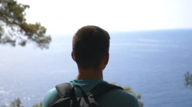 Sırt çantalı erkek yürüyüşçü, tepenin üstünde duruyor ve güzel deniz manzarasına hayran. Seyahatten zevk alan bir adam neşeli duygular ya da mutluluk gösterir. Turist yolculuk boyunca aktif olarak dinleniyor ve özgürlüğün tadını çıkarıyor