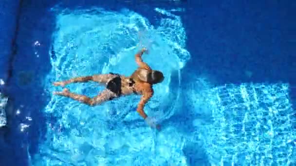 Неузнаваемая красивая девушка в черном купальнике, купающаяся в бассейне роскошного отеля. Молодая женщина отдыхает в теплой воде бассейна и наслаждается летними каникулами. Концепция отдыха. Медленный вид сверху — стоковое видео