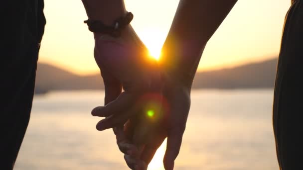 Férfi és női kezek ölelik egymást naplementekor. A fiatal pár a tengerparton áll, és élvezik az együtt töltött időt. Romantikus pillanat két szerető között. A szeretet vagy a boldogság fogalma. Lassabban.