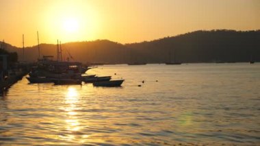 Deniz yüzeyinde yüzen balıkçı teknelerinin güzel manzarası ve arka planda günbatımı. Deniz kıyısının yakınında duran balıkçı gemileri. Altın güneş ışığı okyanus ortamını aydınlatıyor. Manzaralı deniz manzarası