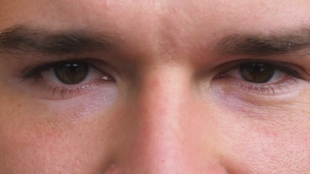 Feche os olhos castanhos do cara olhando e piscando com a visão irritada. Retrato do rosto masculino olhando seriamente para a câmera com emoção negativa. Expressão facial do jovem confiante — Vídeo de Stock